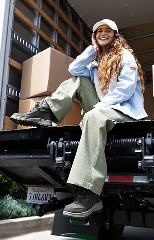 Young woman wearing Roxy work boots and sitting on back of liftgate box truck